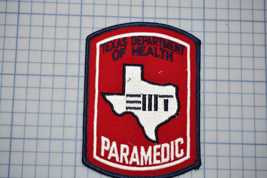 A red and blue Texas Department of Health Paramedic patch is displayed against a grid background.