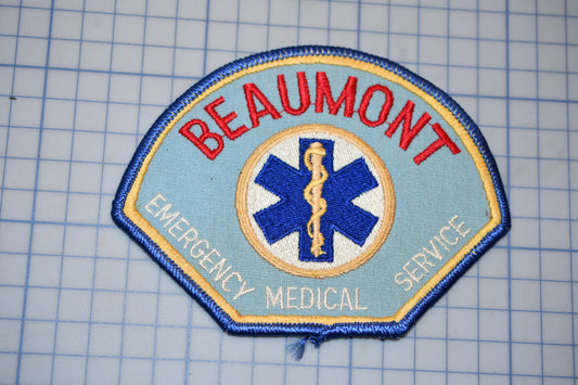 a patch with the text "BEAUMONT EMERGENCY MEDICAL SERVICE" and a medical symbol, likely representing the emergency medical service of Beaumont.