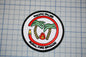 a circular patch with a red border, depicting a firefighting emblem with palm trees and a fire. The patch is labeled "Pacific Palms Rural Fire Brigade".