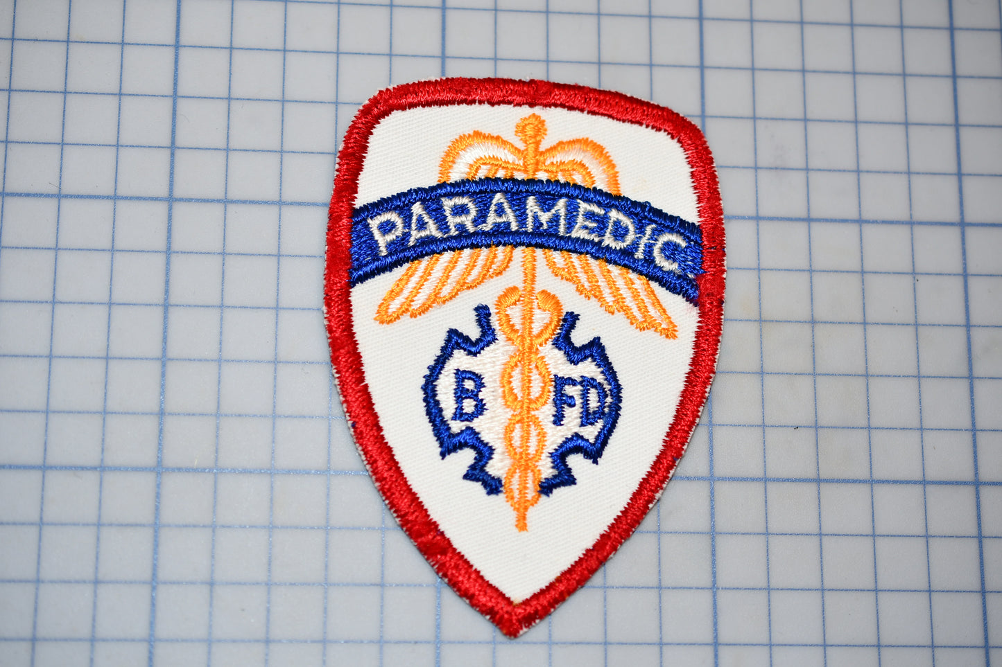 a red and white badge with the word "PARAMEDIC" written on it, along with a medical symbol.