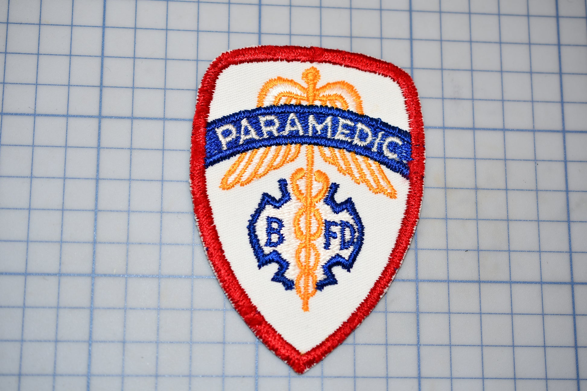 a red and white badge with the word "PARAMEDIC" written on it, along with a medical symbol.