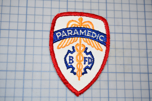 a red and white badge with the word "PARAMEDIC" written on it, along with a medical symbol.