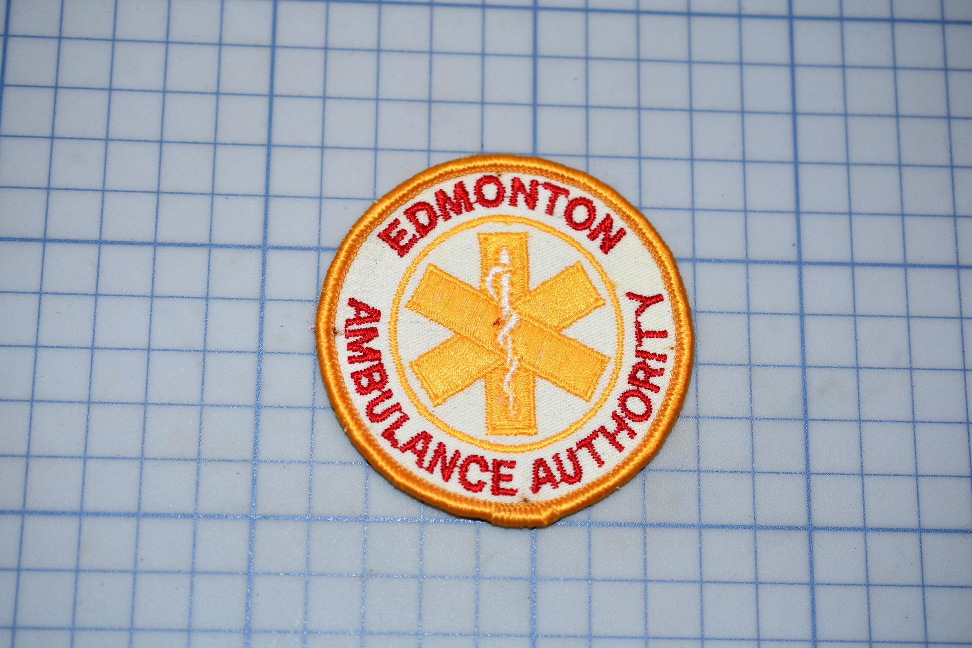 a patch with the text "EDMONTON AMBULANCE AUTHORITY" and a symbol of a cross, which is a common emblem associated with emergency medical services.