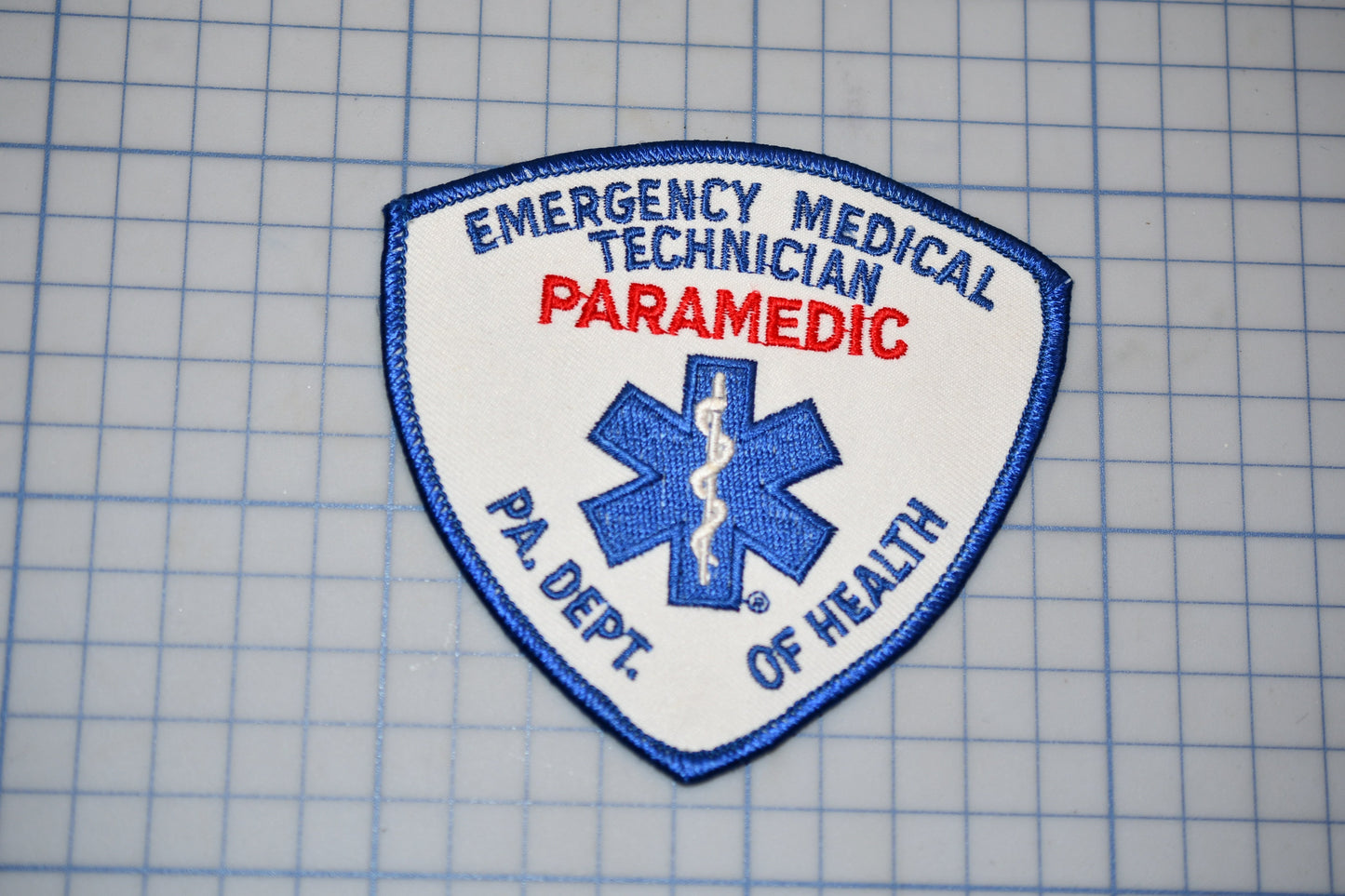 a patch with the text "EMERGENCY MEDICAL TECHNICIANS PARAMEDIC" and a medical symbol, indicating that it is a patch for an emergency medical technician or paramedics.