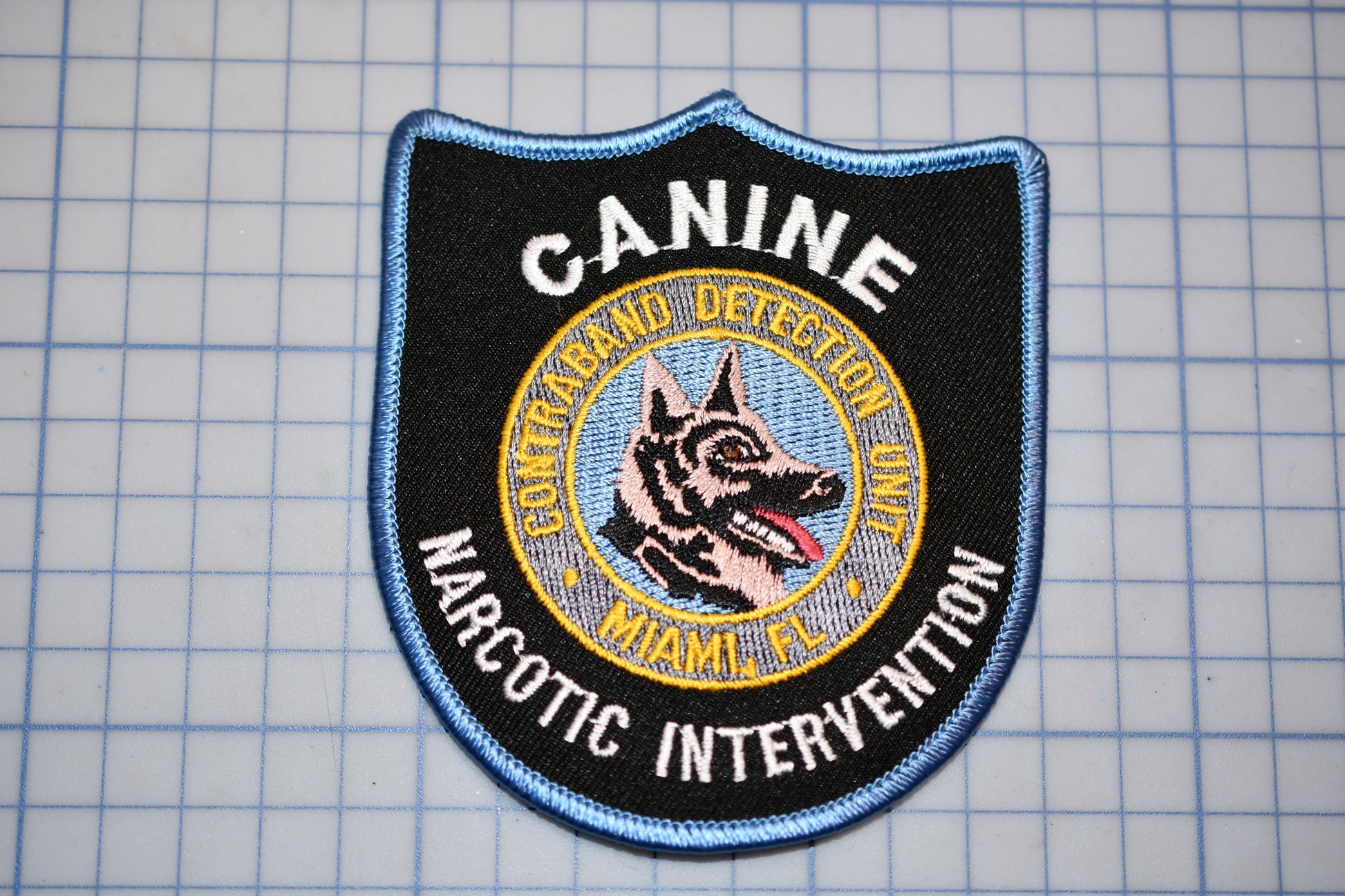 A black and blue patch with the text "CANINE DETECTION UNIT" and "NARCOTIC INTERVENTION" printed on it, along with a graphic of a dog's head.