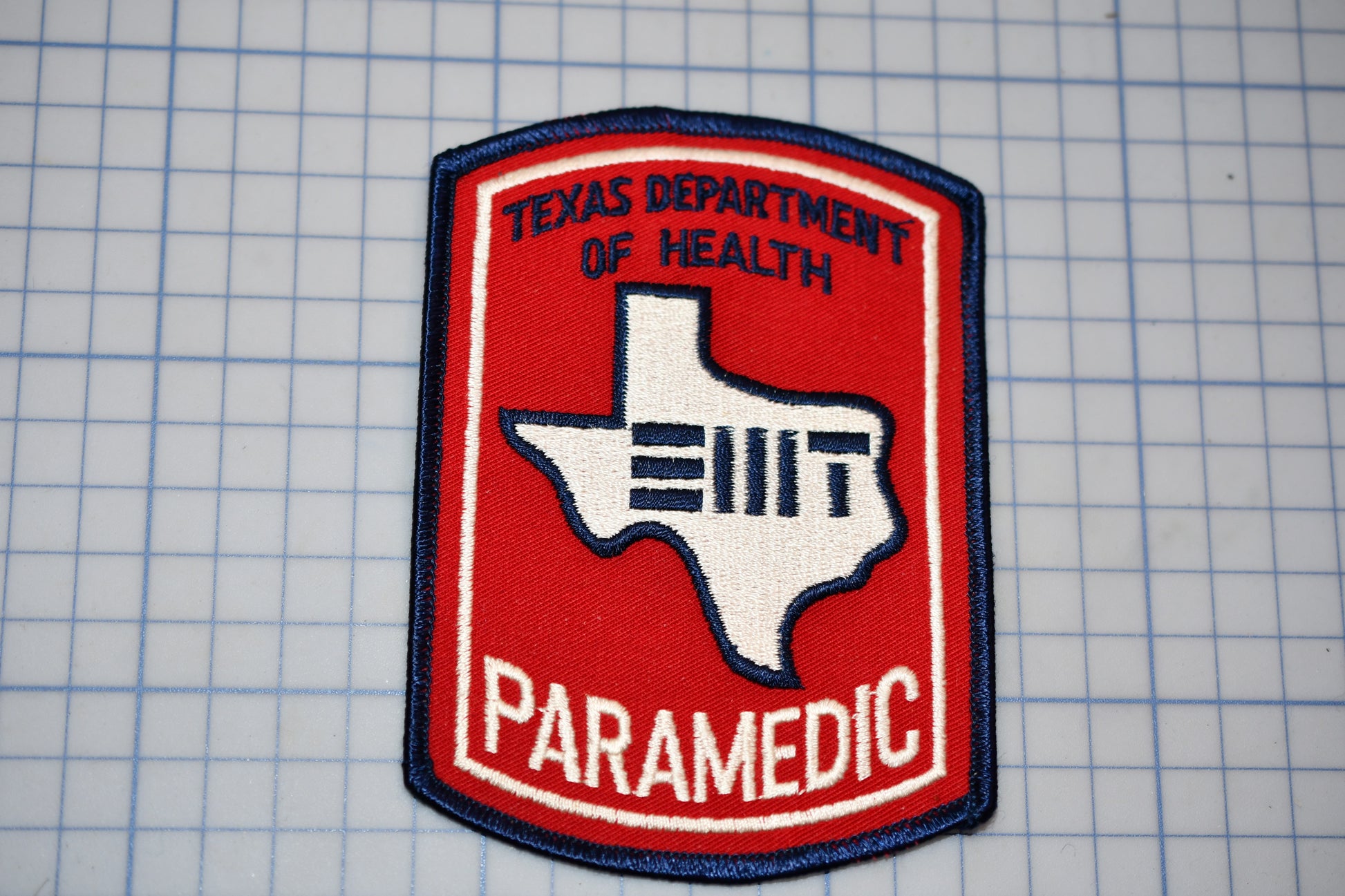 A Texas Department of Health Paramedic (TDAHP) patch is displayed against a grid background.