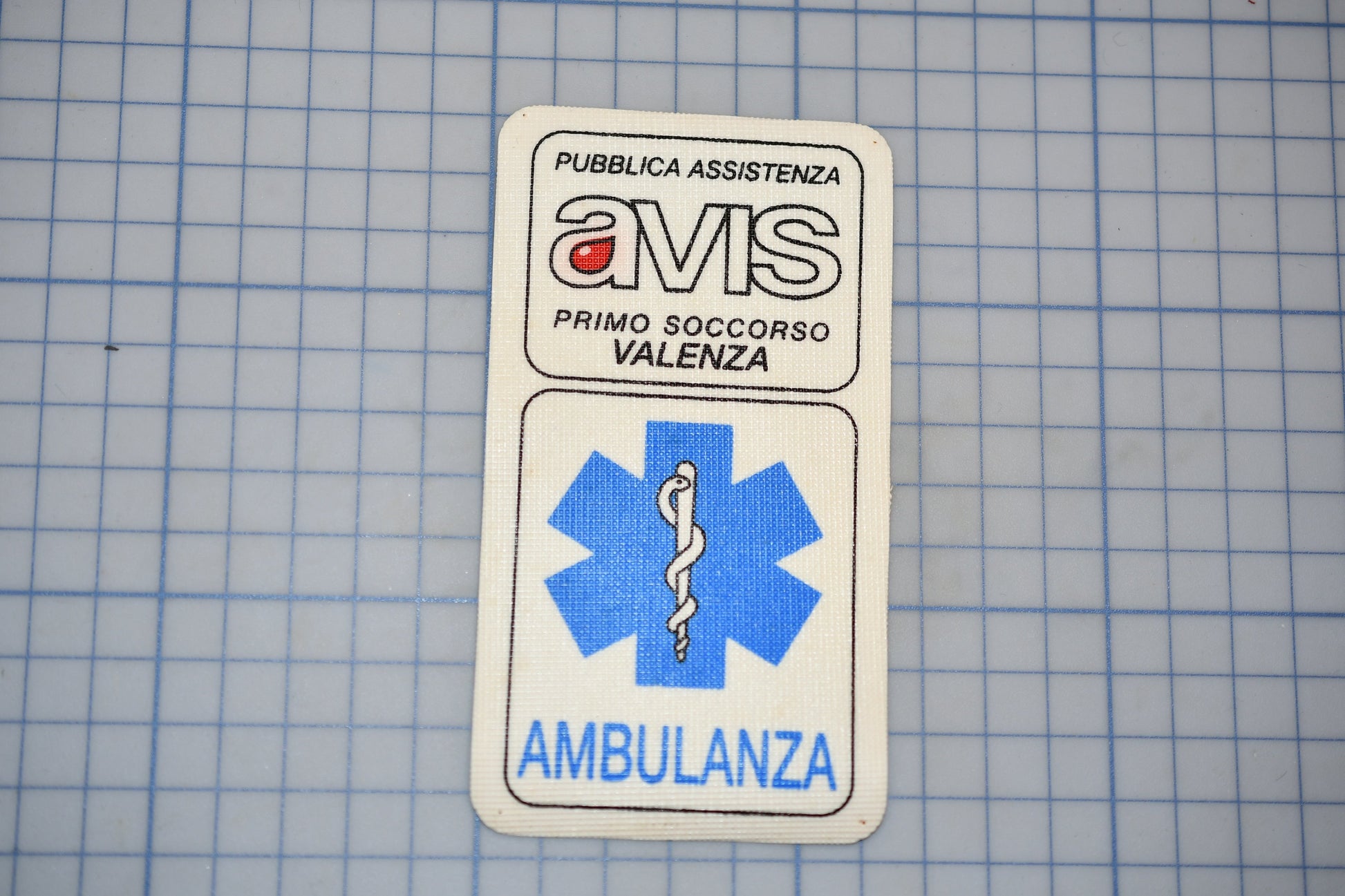 a white patch with text and a medical symbol, placed on a blue grid background.