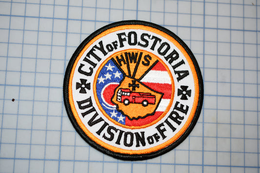 a circular patch with a design that includes a fire truck, stars, and the text "City of Fostoria Division of Fire".