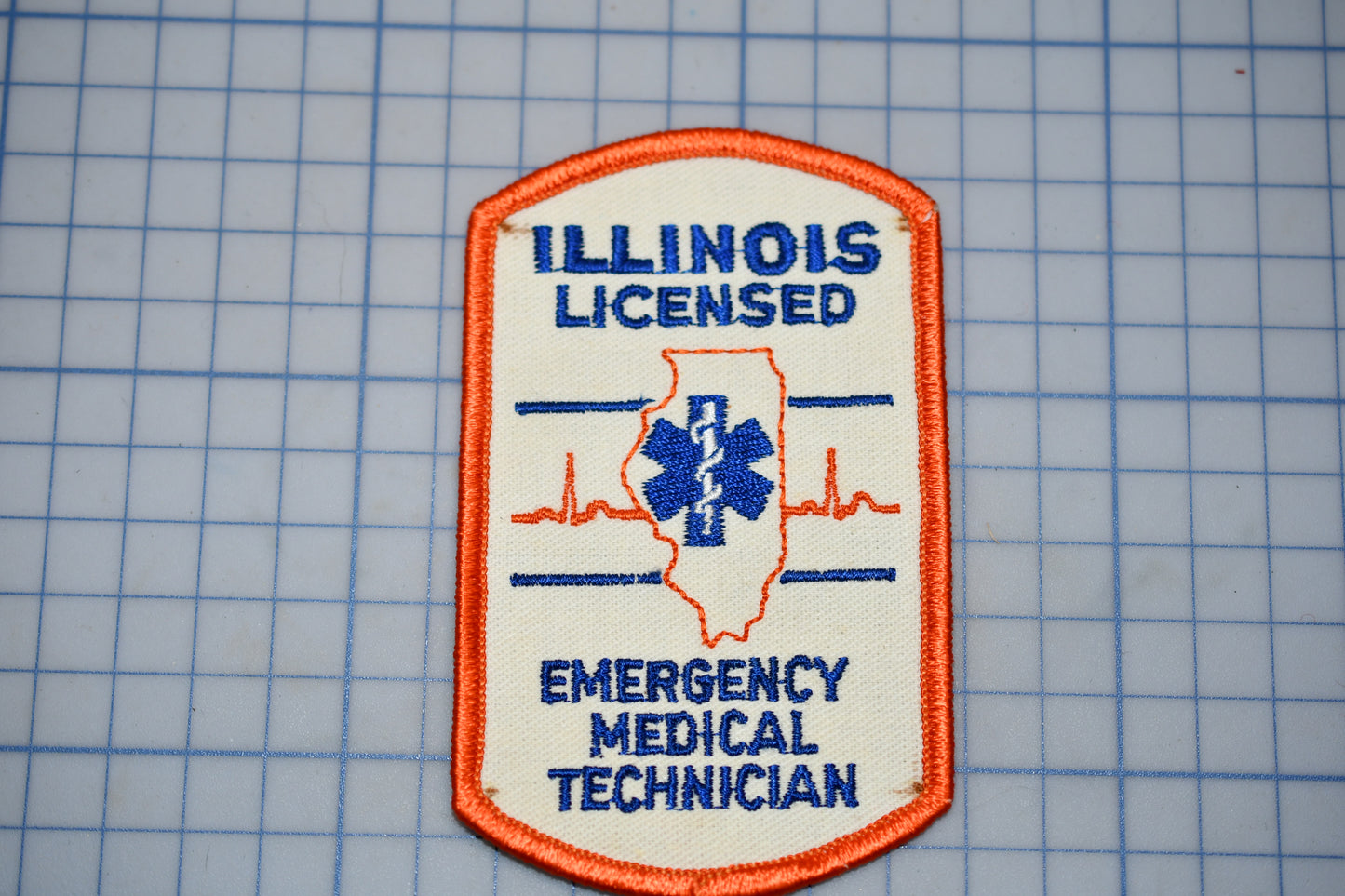 a patch with the text "ILLINOIS LICENSED EMERGENCY MEDICAL TECHNICIAN" and a medical symbol, indicating that the person is an Illinois Emergency Medical Technician.