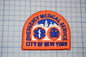 a patch with the text "EMERGENCY MEDICAL SERVICE CITY OF NEW YORK" and two medical symbols, one of which is a cross and the other a stethoscope.