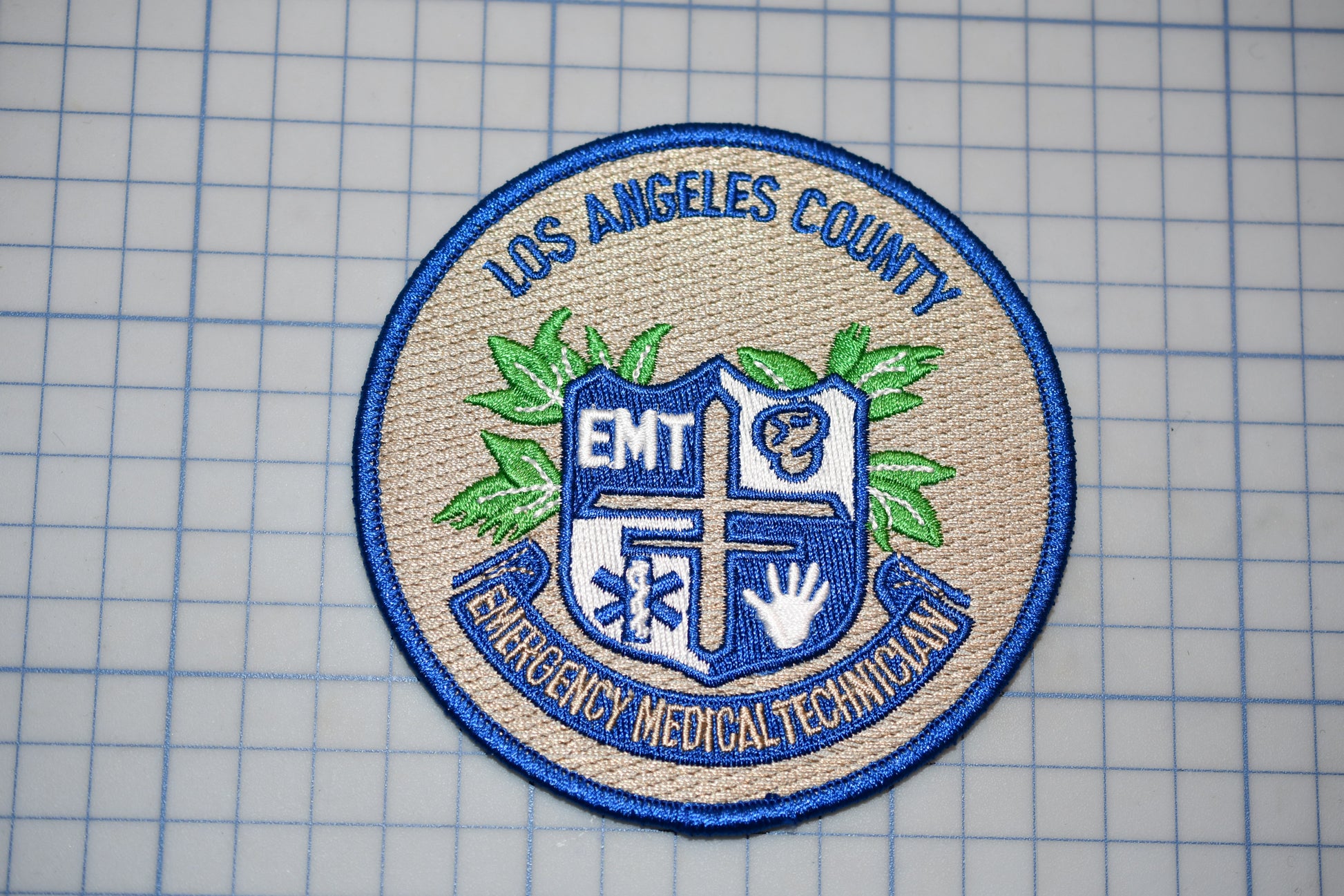a badge or patch with the text "Los Angeles County EMT Emergency Medical Technician" and a shield-like emblem with a cross and leaves.