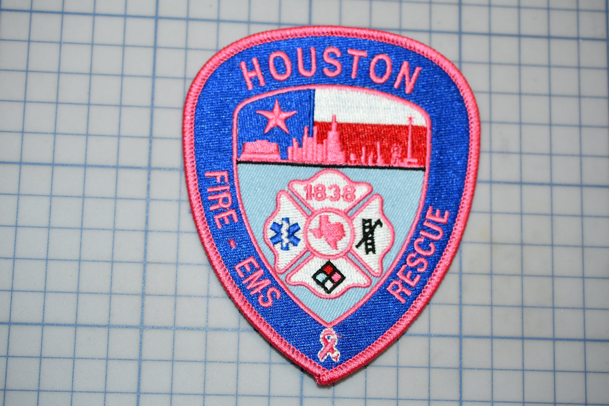 A patch with the text "HOUSTON FIRE - EMERGENCY RESCUE" and a shield-shaped emblem featuring a city skyline, a fireman's helmet, and a ribbon symbol.