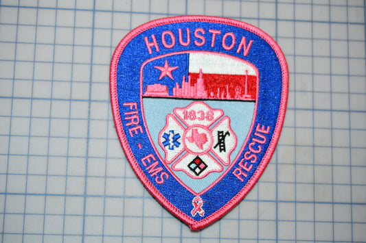 A patch with the text "HOUSTON FIRE - EMERGENCY RESCUE" and a shield-shaped emblem featuring a city skyline, a fireman's helmet, and a ribbon symbol.