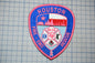 A patch with the text "HOUSTON FIRE - EMERGENCY RESCUE" and a shield-shaped emblem featuring a city skyline, a fireman's helmet, and a ribbon symbol.