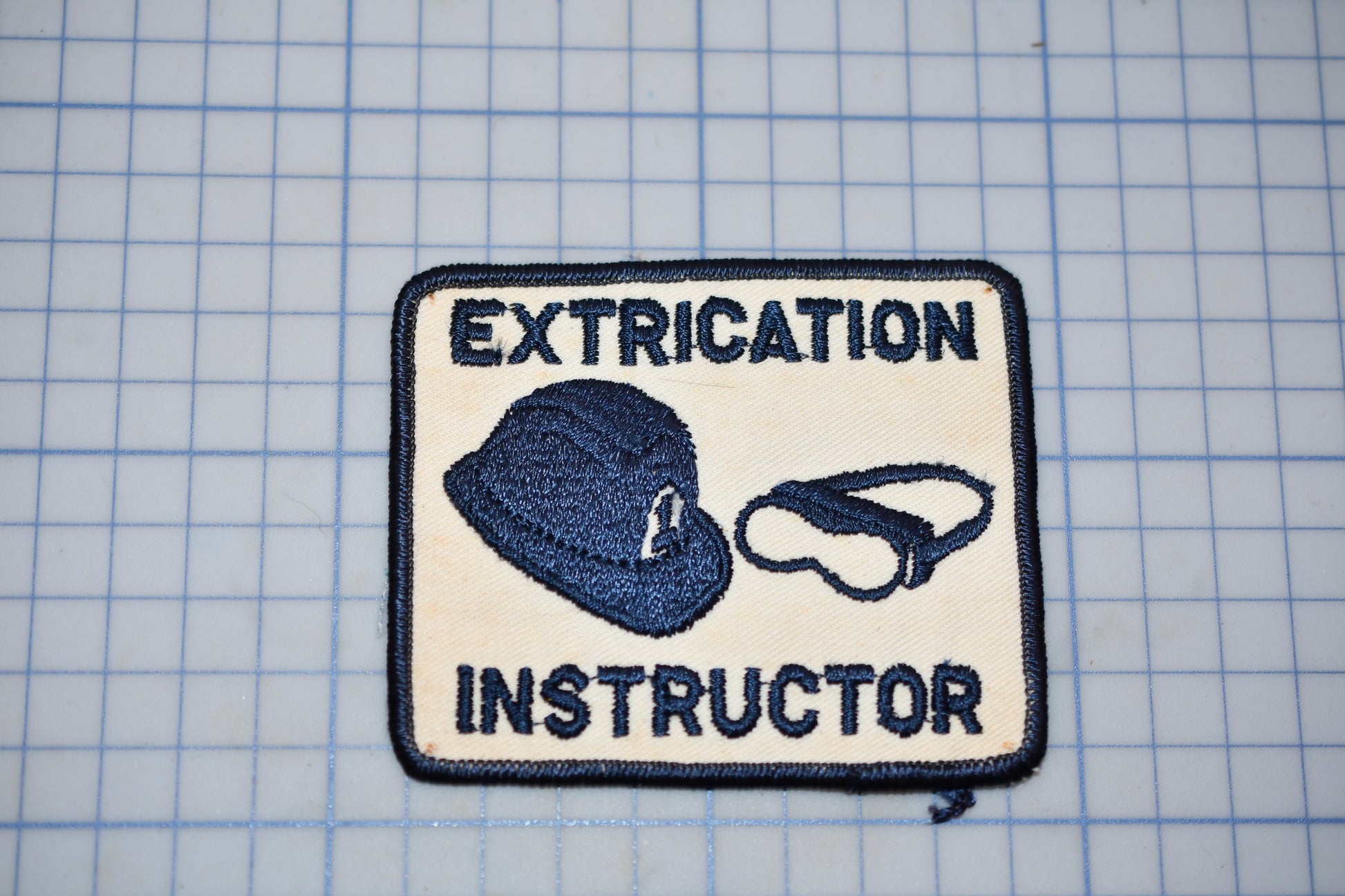 a patch with the text "EXTRICATION INSTRUCTOR" and an illustration of a hat and a pair of goggles.