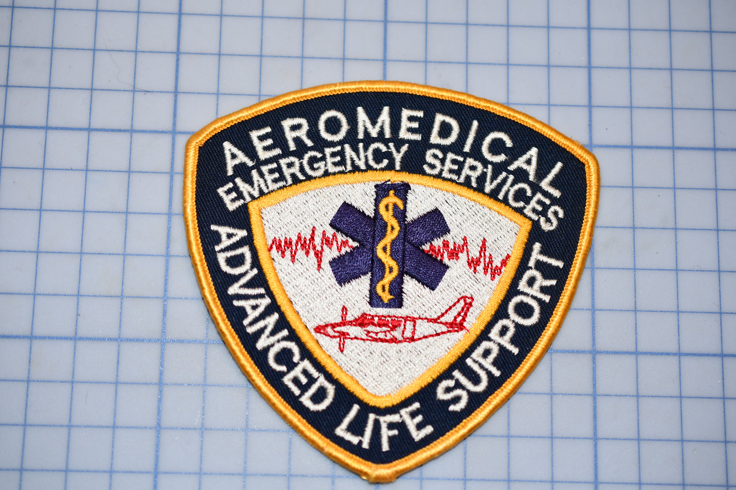 a patch with the text "AEROMEDICAL EMERGENCY SERVICES ADVANCED LIFE SUPPORT" and a medical symbol, indicating that it is a patch representing the emergency medical services of an organization.