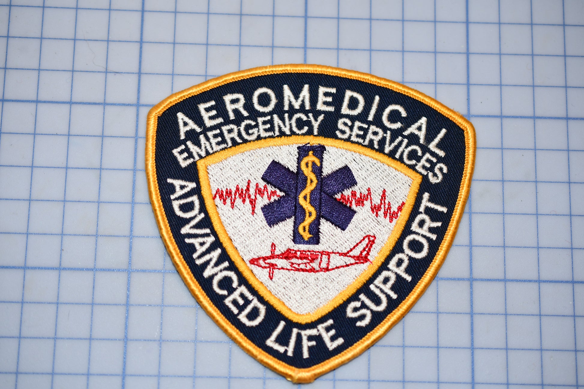 a patch with the text "AEROMEDICAL EMERGENCY SERVICES ADVANCED LIFE SUPPORT" and a medical symbol, indicating that it is a patch representing the emergency medical services of an organization.