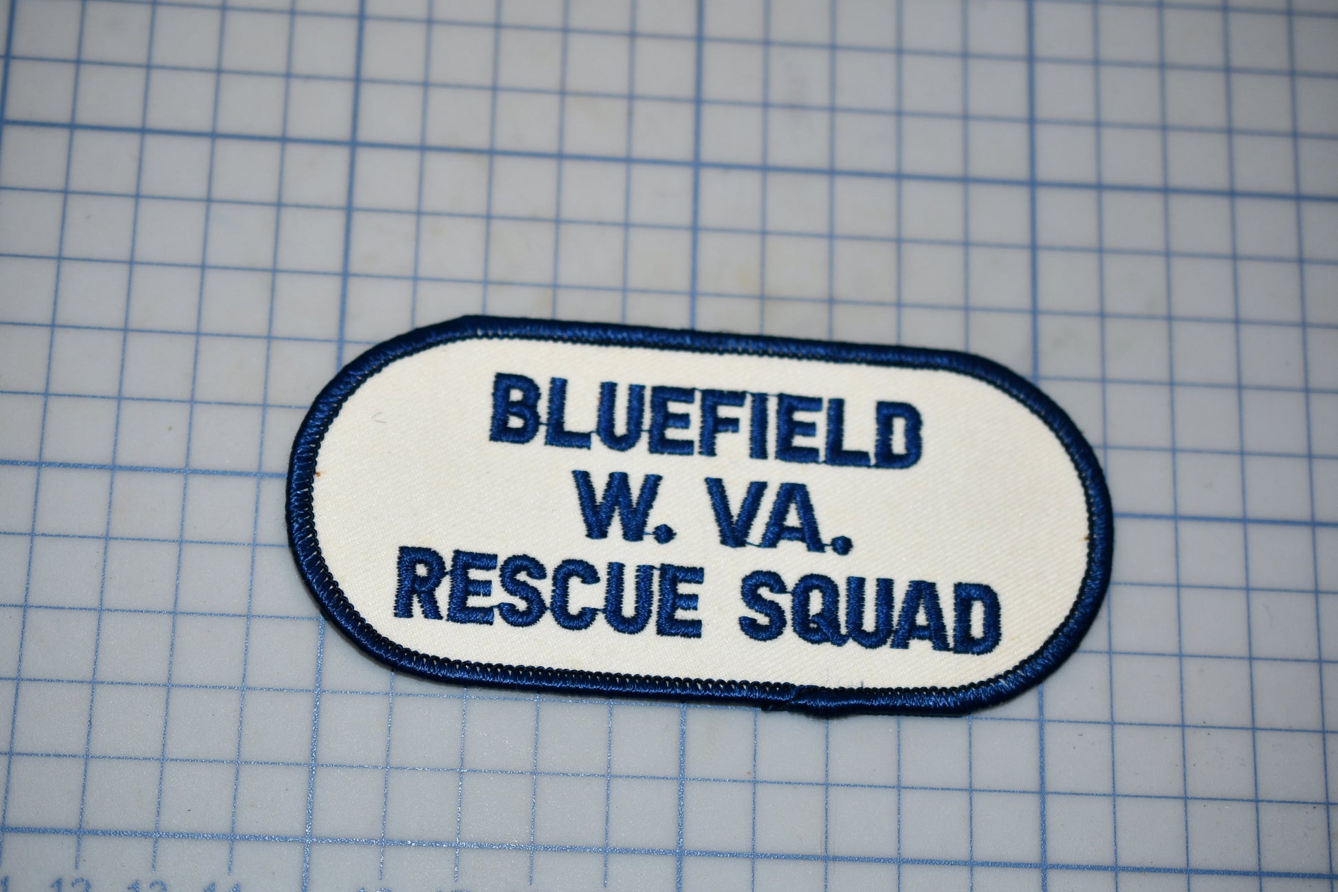 A patch with the text "BLUETFIELD W. VA. RESCUE SQUAD" printed on it, indicating that it is a patch from the Bluefield Rescue Squad.