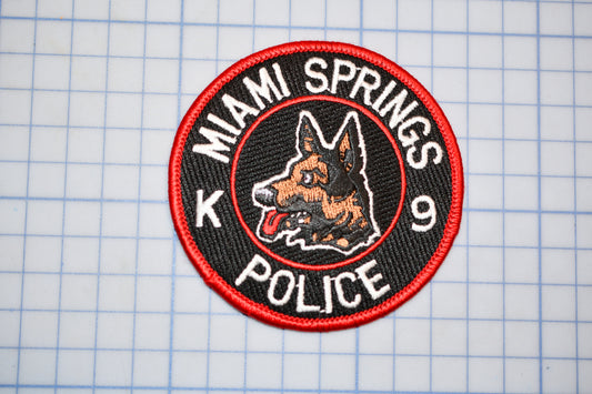 A red and black patch with a dog's head and the text "MIAIM SPRINGS POLICE" printed on it.