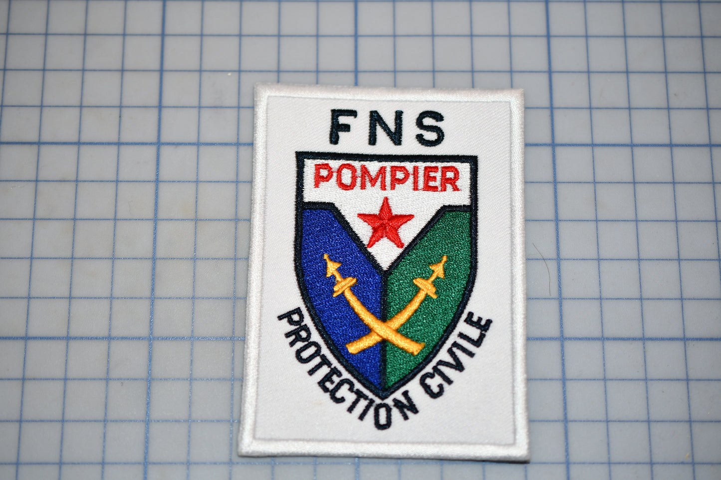 a white patch with the text "FNS Pompier Protection Civille" and a crest with a star and crossed swords.