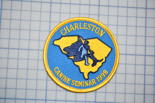 A patch with the text "CHARLESTON" and "CANNINE SEMINAR 1998" on it, along with a map of South Carolina and a silhouette of a person walking.