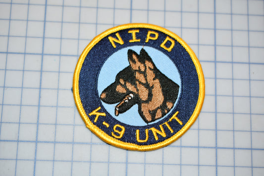 A circular patch with a dog's head and the text "NIPD K-9 UNIT" printed on it, placed on a grid background.