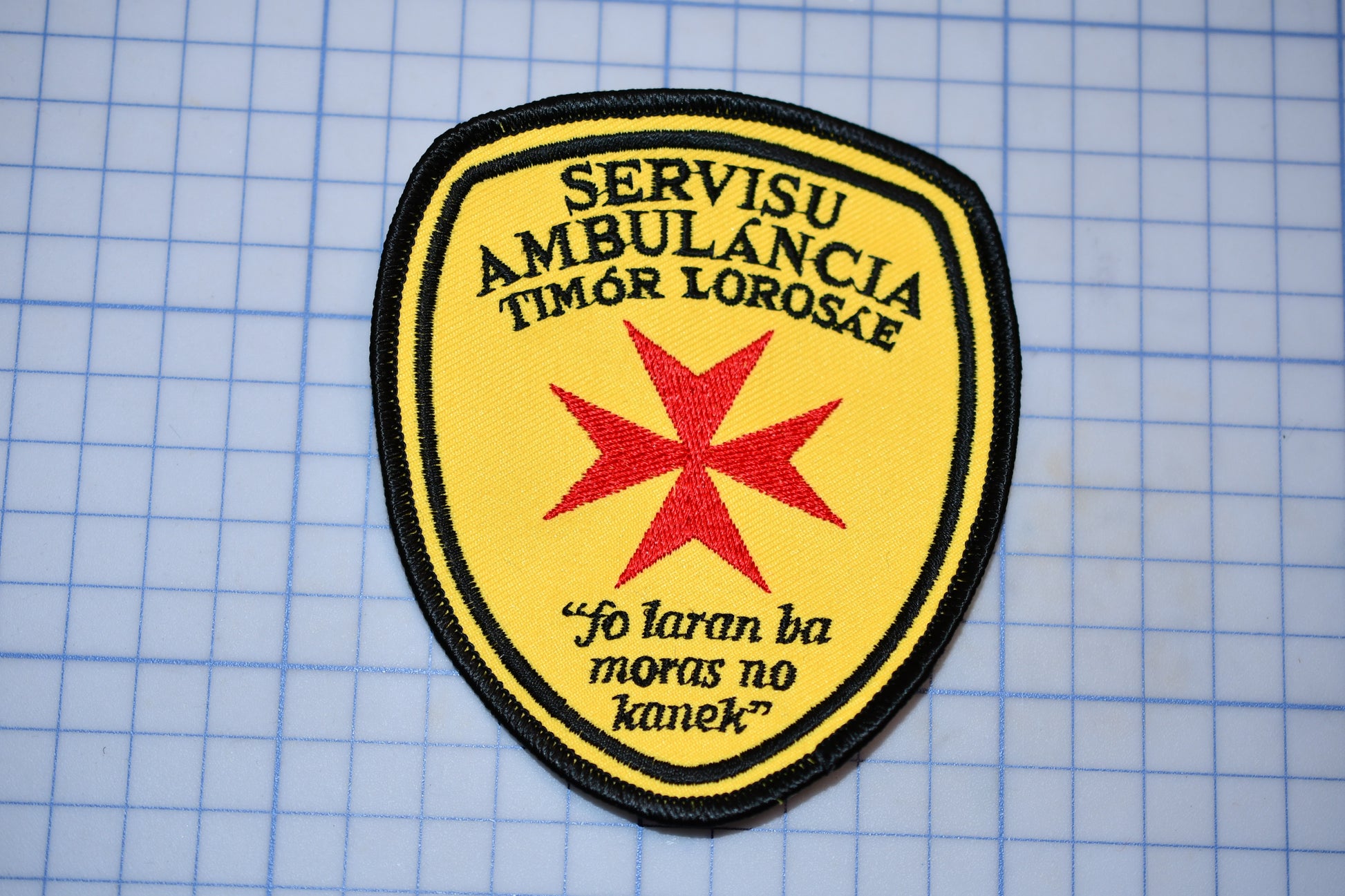 a yellow and black patch with a red star and text, placed on a blue grid background.
