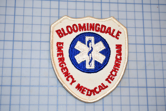 a patch with the text "Bloomingdale Emergency Medical Technician" and a medical symbol, indicating that it is a badge or patch representing the emergency medical technician program in the town of Bloomingdale.