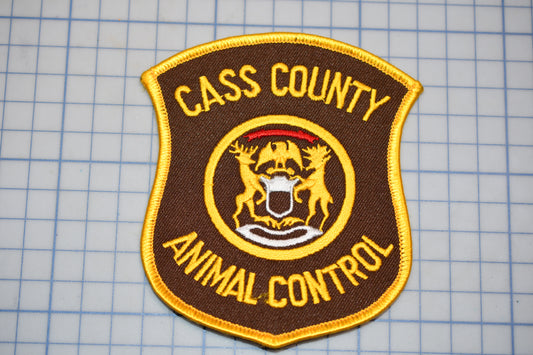 A brown and gold patch with the text "CASS COUNTY ANIMAL CONTROL" and a coat of arms, indicating the presence of an animal control service.
