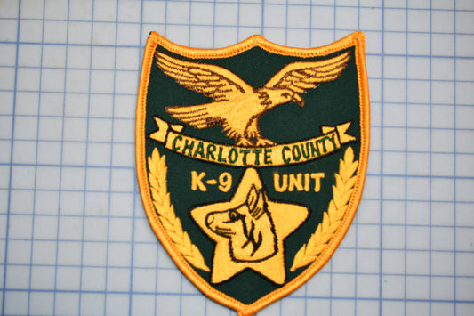A shield-shaped badge with a bird, a dog, and text, likely representing a K-9 unit or a similar organization.