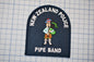 a patch with a cartoon character playing a musical instrument, specifically a pipe. The patch is labeled "New Zealand Police Pipe Band".