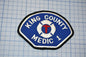 A blue and white patch with the text "KING COUNTY MEDIC 1" and a medical symbol, likely representing a medical emergency response team.