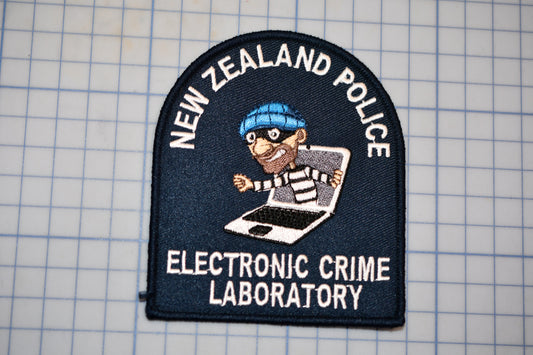 a patch with the text "NEW ZEALAND POLICE ELECTRONIC CRIME LABORATORY" and an illustration of a person wearing a blue hat and holding a laptop.
