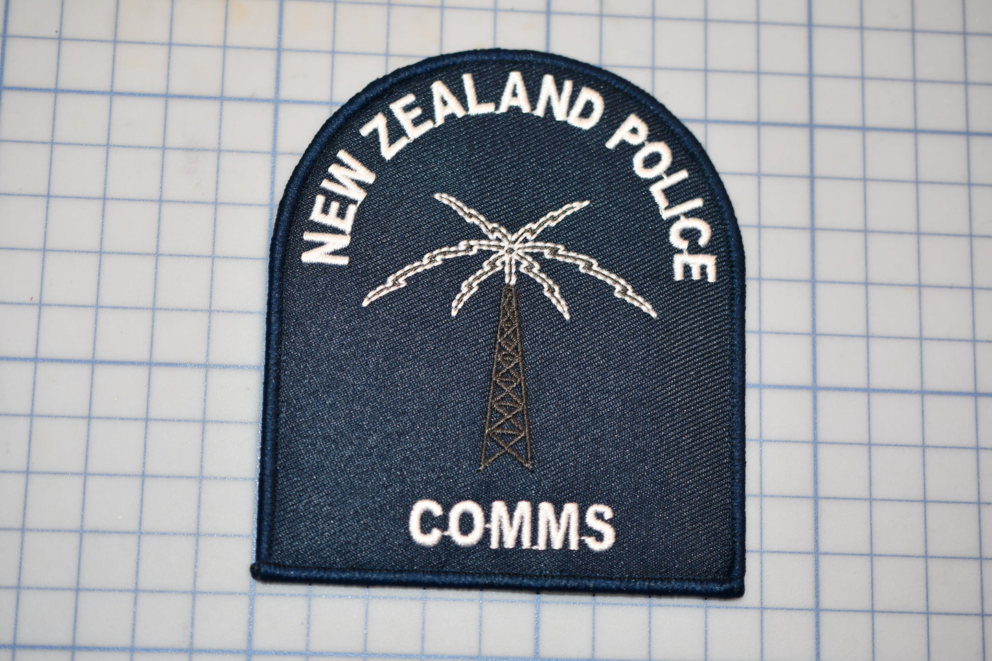 a New Zealand Police patch with a palm tree and a radio tower, along with the text "NEW ZEALAND POLICE" and "COMM".