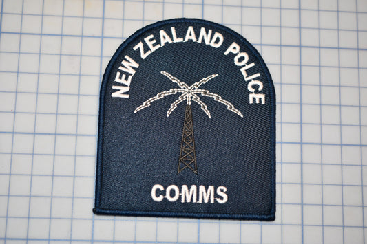 a New Zealand Police patch with a palm tree and a radio tower, along with the text "NEW ZEALAND POLICE" and "COMM".