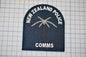 a New Zealand Police patch with a palm tree and a radio tower, along with the text "NEW ZEALAND POLICE" and "COMM".