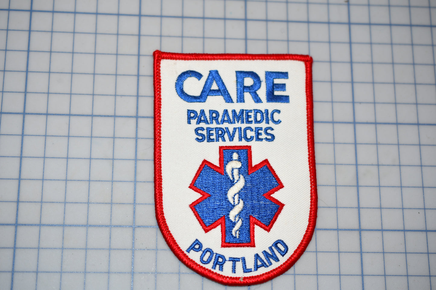 a patch with the text "CARE PARAMEDIC SERVICES PORTLAND" and a medical symbol, likely representing a healthcare organization or institution.