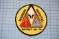 a circular patch with a design that includes a triangle, a symbol, and text. The patch is placed on a grid background.