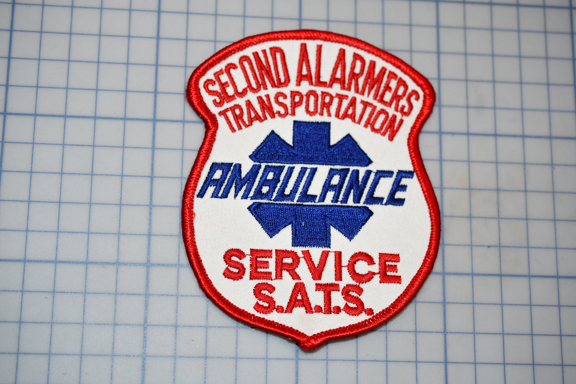 a red and white patch with the text "Second Ambulance Service" and "Ambulance Service S.A.T.S."