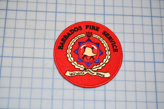 A red circular patch with the text "BARRADOS FIRE SERVICE" and a red emblem featuring a bell and a star, placed on a grid background.