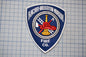 a blue and white patch with a firefighting emblem, including a fire hydrant, a fireman's helmet, and a firetruck. The patch is displayed against a grid background.