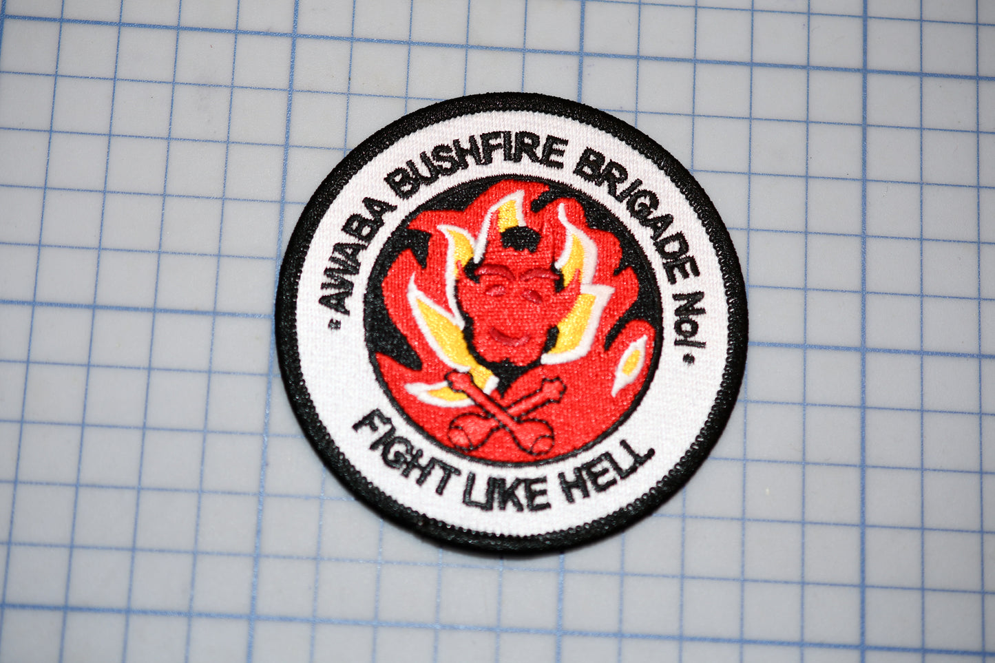 a circular patch with a red devil-like figure and flames, surrounded by the text "ANNABAA BUSHFIRE BRIGADE No.1 - FIGHT LIKE HELL".