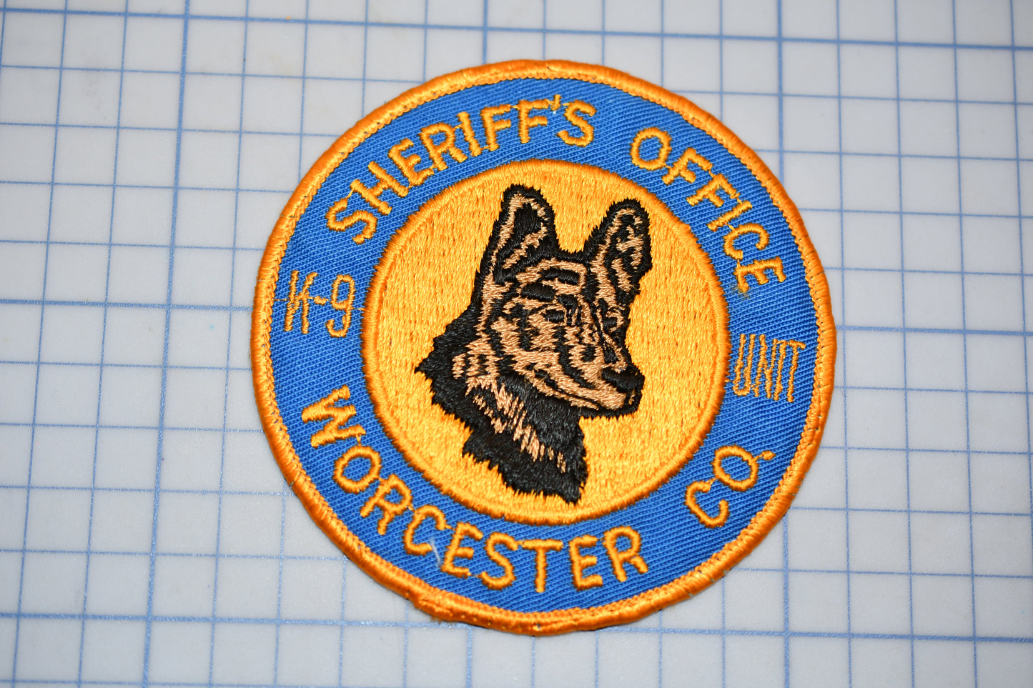 A patch with a dog's head and the text "Sheriff's Office" around it, placed on a grid background.