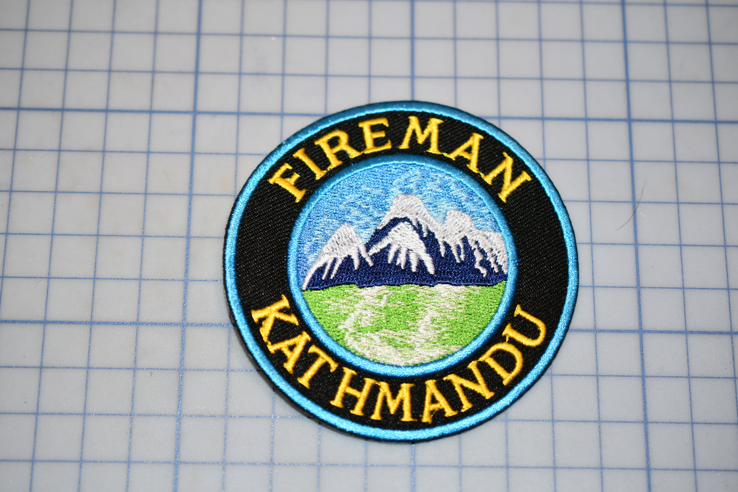 a circular badge with a mountain landscape and the text "FIREMAN KATHMANDU" around the edge.