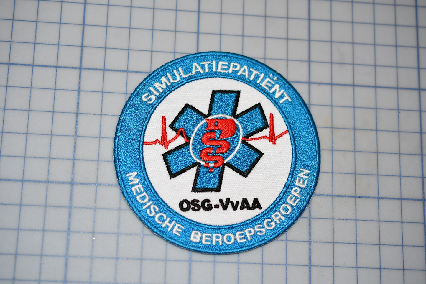 a blue and white patch with a medical symbol and text, placed on a grid background.