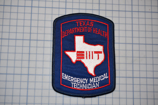 A Texas Department of Health Emergency Medical Technician (EMT) patch is displayed against a grid background.