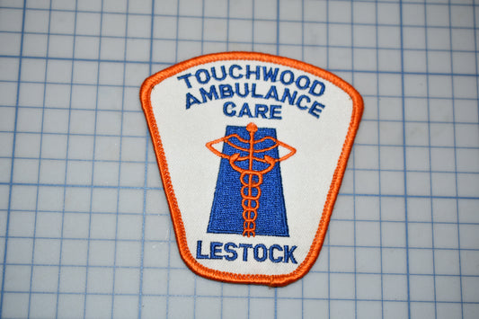 a patch with the text "TOUCHWOOD AMBULANCE CARE LESSTOCK" and an emblem depicting a medical symbol.