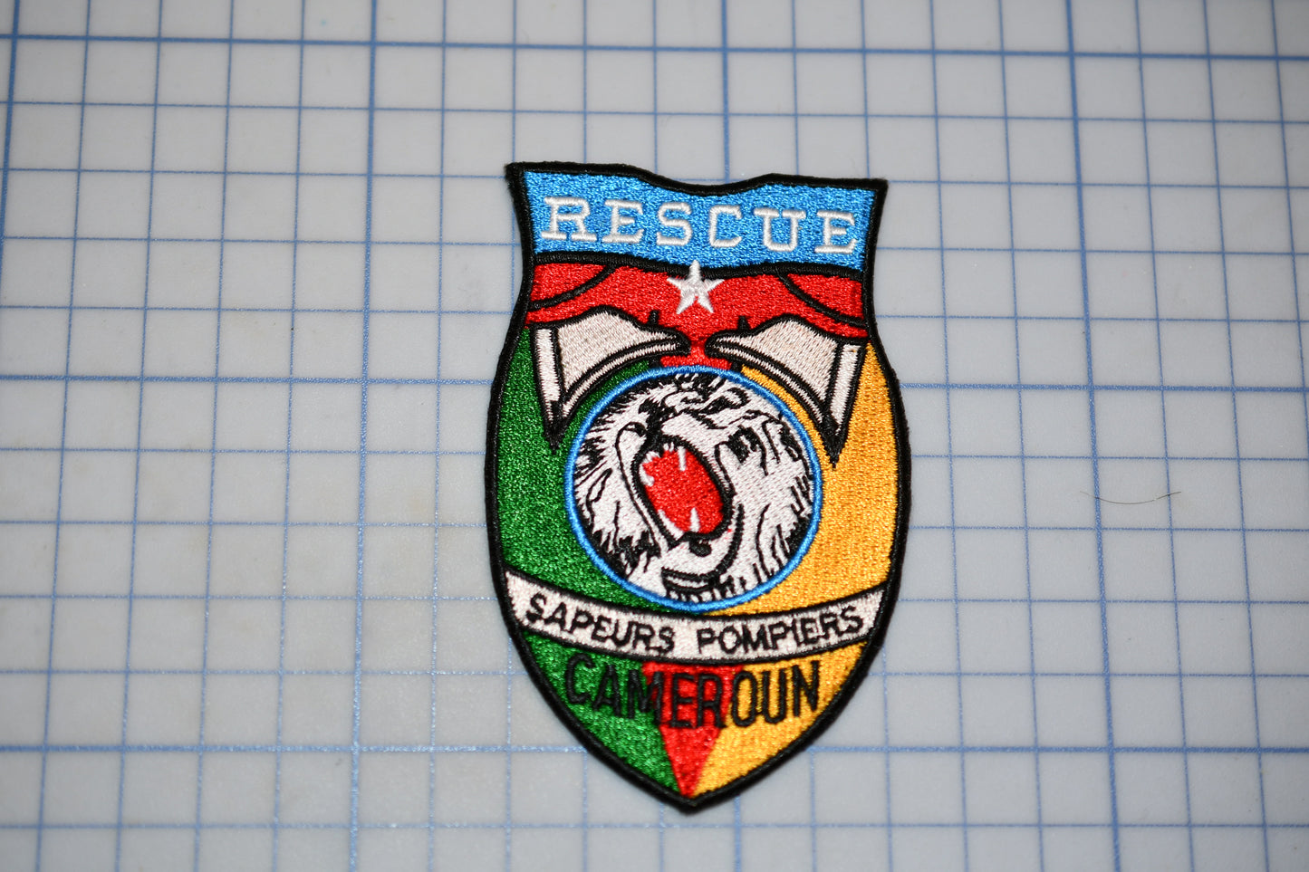 a colorful patch with the word "RESCUE" prominently displayed, along with a lion and the text "SAÊURE'S POMPIERS" and "CAMEROUN".