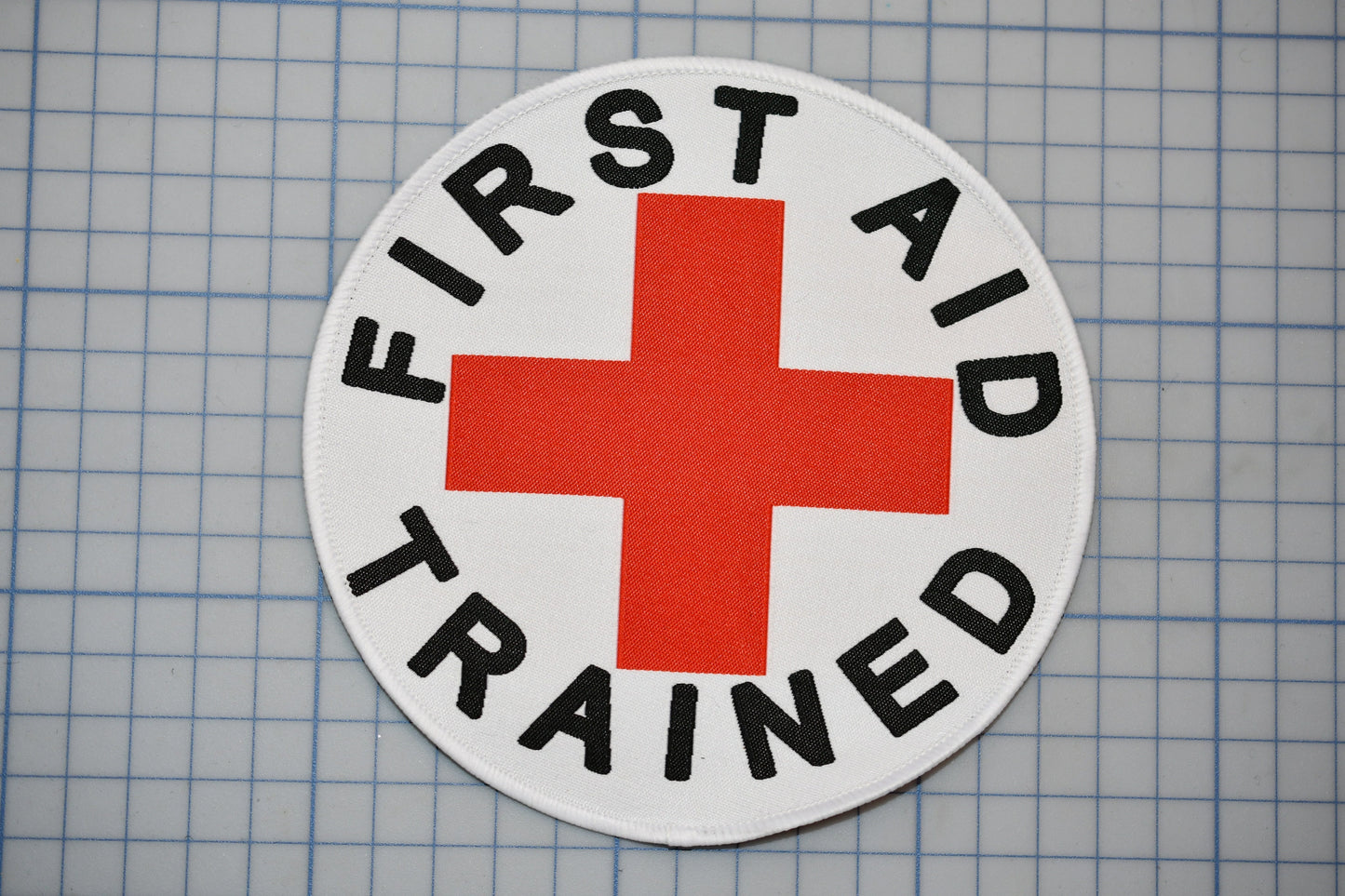 A white circle with a red cross and the text "FIRST AID TRAINED" printed on it.