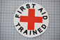 A white circle with a red cross and the text "FIRST AID TRAINED" printed on it.